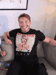 a man wearing a playboy t-shirt is sitting on a couch with his arms outstretched