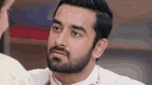 a man with a beard wearing a white shirt looks at a woman