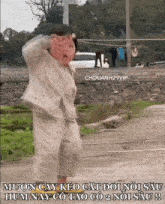 a little girl is standing on a dirt road in front of a stone wall and making a face .