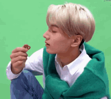 a young man wearing a green sweater is eating a snack .