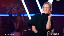a woman is sitting in a chair with a nbc logo in the background