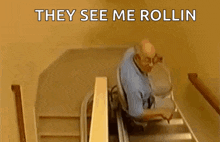 a man in a wheelchair is going up a set of stairs with the words they see me rollin above him .