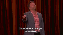 a man in a suit and plaid shirt is standing on a stage and says `` now let me ask you something ! ''