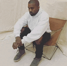 a man in a white hoodie sits on a chair with his legs crossed