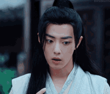 a man with long black hair and a ponytail is wearing a white shirt and a blue vest .