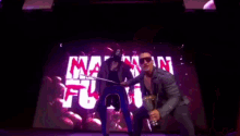 a man in a leather jacket and sunglasses is holding a trophy in front of a large screen with the word mafia on it
