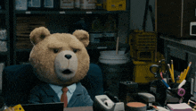 a teddy bear in a suit sits at a desk