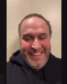 a man with a beard and a black hoodie is smiling .