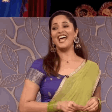 a woman wearing a blue top and a green saree is smiling