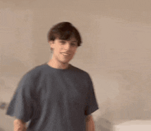 a young man wearing a blue t-shirt is standing in front of a wall and smiling .