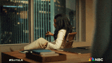 a woman sits at a desk with a nbc logo on the bottom right