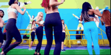 a group of women are dancing on a field in front of a blue wall .