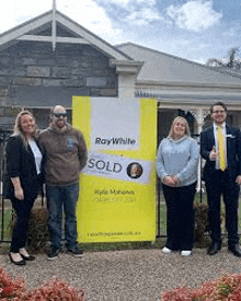 a group of people standing in front of a house with a sold sign .