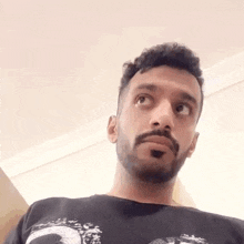 a man with a beard and mustache is wearing a black t-shirt and looking up .