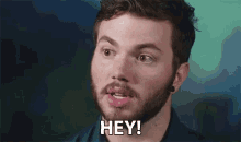 a man with a beard is making a funny face and saying hey !