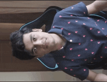 a young man wearing a blue shirt with pink birds on it sits in a chair