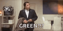 a man in a suit is standing in a living room holding a jacket and saying `` green ? '' .