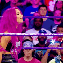 a woman with pink hair is standing in a wrestling ring in front of a crowd of people .