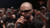 a bald man wearing sunglasses is singing into a microphone