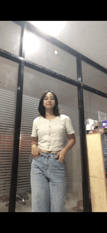a woman in a white shirt and blue jeans stands in front of a glass wall