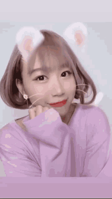 a woman wearing a purple sweater and white ears looks at the camera