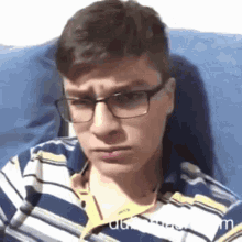 a man wearing glasses and a striped shirt is sitting on a couch .