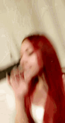 a blurry picture of a woman with red hair drinking from a glass .