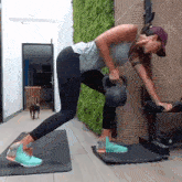 a woman is lifting a kettlebell on a mat while a dog looks on