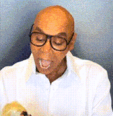 a bald man wearing glasses and a white shirt has his tongue out