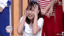 a girl is covering her ears with her hands and smiling while standing in front of a group of people .