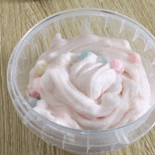 a clear bowl filled with pink frosting and candy on a table