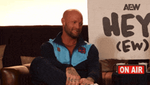 a man sits on a couch in front of a sign that says hey