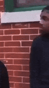two people are standing in front of a brick wall .