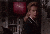 a woman in a blue jacket stands in front of a bookshelf with a bell on it