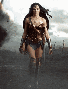 a woman in a wonder woman costume is walking in a field holding a sword and shield .