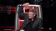 a man is sitting in a chair with his fist in the air and the words nbc on the bottom
