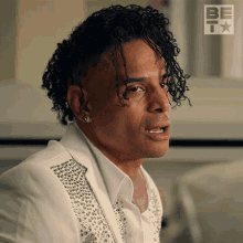 a man with curly hair is wearing a white shirt with silver studs on it