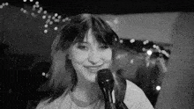 a woman is singing into a microphone and smiling in a black and white photo .