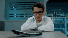 a young man wearing glasses sits at a table