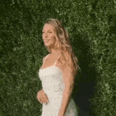 a woman in a white dress is walking in front of a hedge .