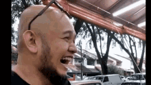 a bald man with a beard is laughing with his mouth open in a parking lot .