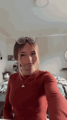 a woman wearing sunglasses and a necklace takes a selfie in a bedroom
