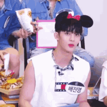 a young man wearing a mickey mouse headband and a name tag is sitting in a chair .