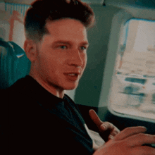 a man in a black shirt is sitting in a car looking out the window and smiling .
