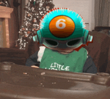 a little boy wearing a green shirt that says little sitting in front of a christmas tree