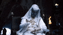 a man dressed as a nun is sitting in a chair reading a book .
