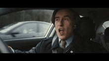 a man in a suit and tie is yawning while driving a car
