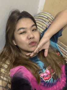 a woman laying on a bed with her eyes closed wearing a tie dye shirt