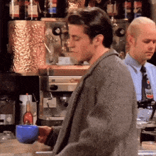 a man is holding a blue cup of coffee in front of a coffee machine