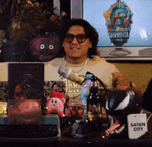 a man sitting in front of a television with a sign that says satan city